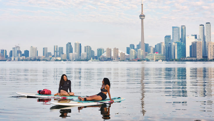 Two women rest on stand up paddle boards in Toronto's harbour.