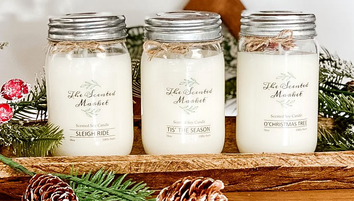 Three scented candles sit on a table decorated for the holidays.