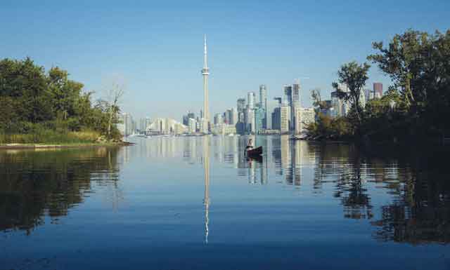 A man canoeing on a river with the Toronto cityscape behind him