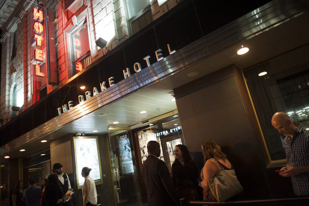 Un groupe de personnes rassemblées devant l’hôtel Drake en soirée.