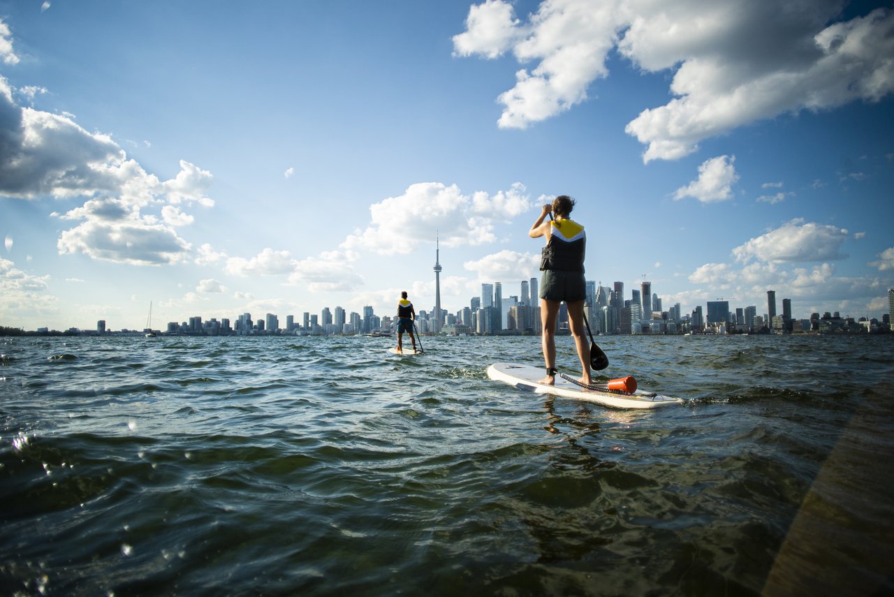 Zwei Personen stehen beim Stand-Up-Paddle-Boarding auf dem Ontariosee, im Hintergrund die Skyline von Toronto