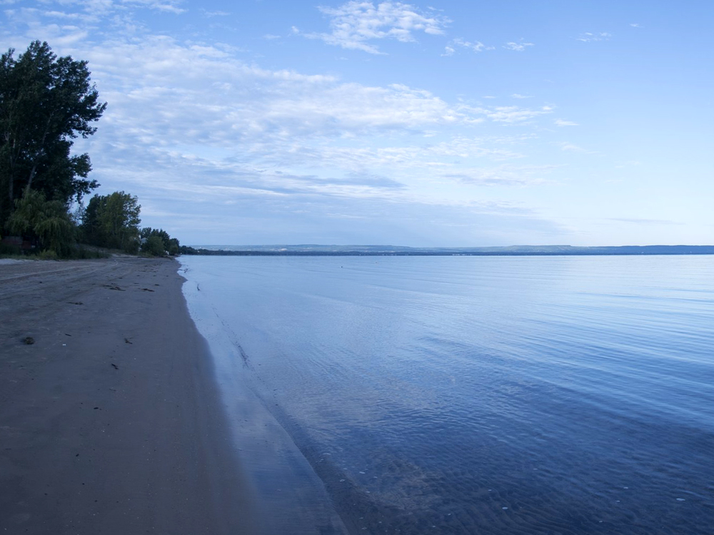 A sandy beach shoreline meets the calm blue waters of Georgian Bay.