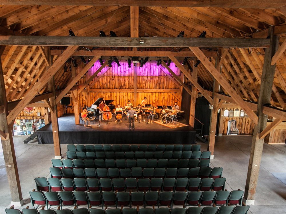 A musical group prepares for a show on stage in a barn venue.