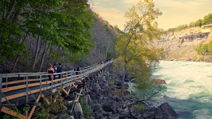 People walking along a boardwalk beside whitewater rapids